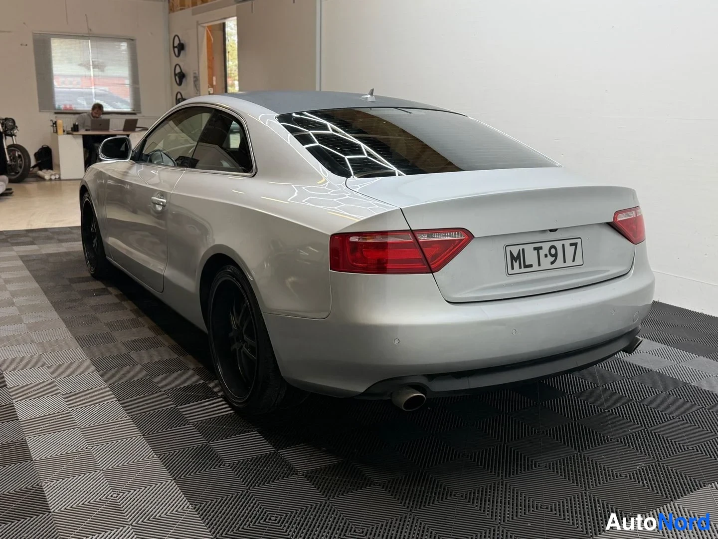 Takaviisto: Audi A5 -coupé, hopeanvärinen, kuvattu takaa viistosti oikealta; rekisterikilpi, mustat vanteet ja tumma katto.