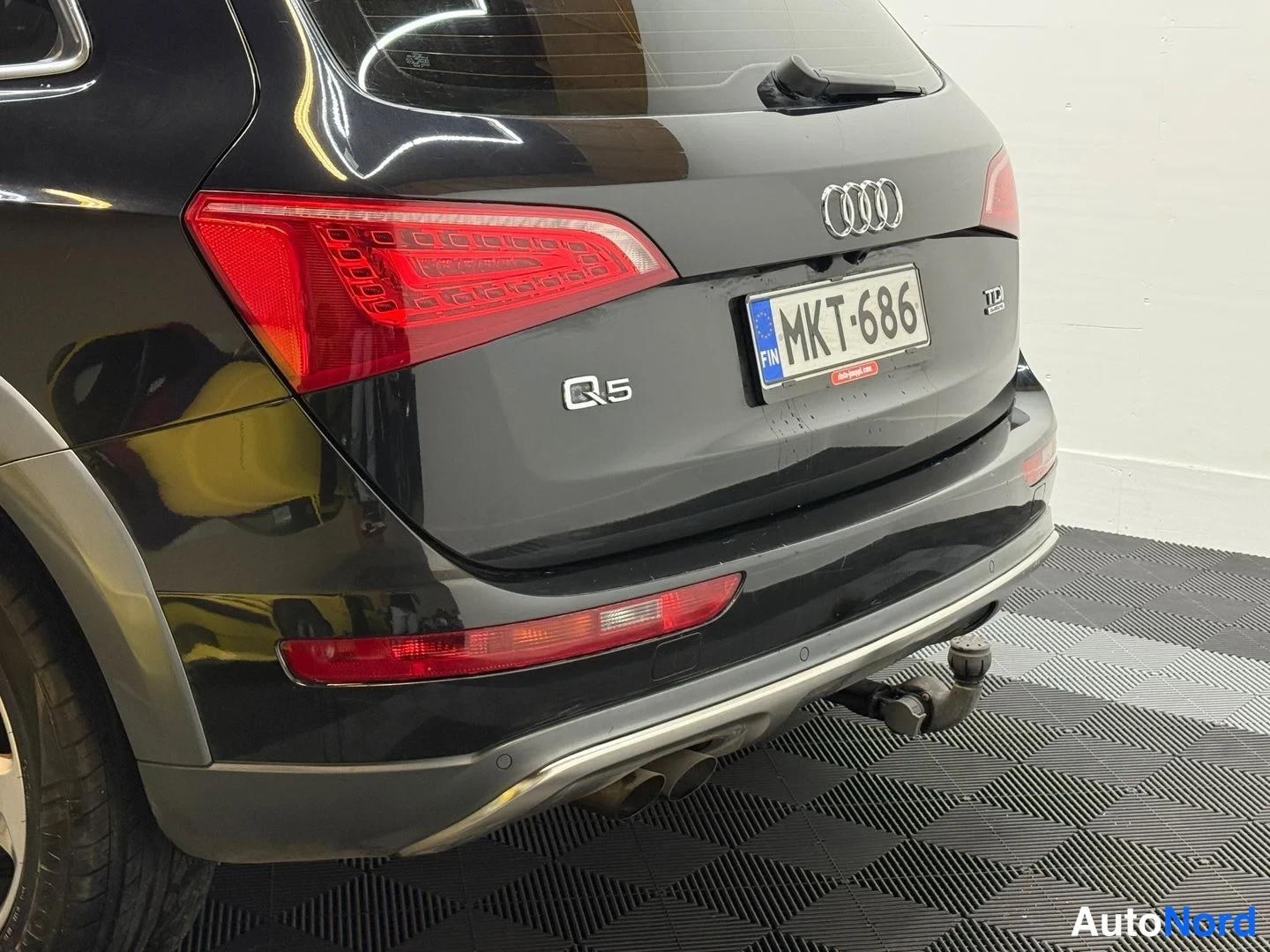 Takaa: Sivutakaan kuvattu musta Audi Q5; tumma lattiamatto autotallin lattialla.