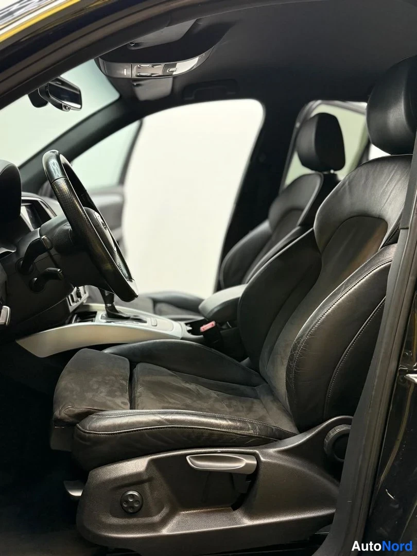Muu: Autoa sisältä: ohjaamo, jossa mustat nahka-suede-etupenkit, ohjauspyörä ja autotallin valkoinen tausta ovista näkyvissä.