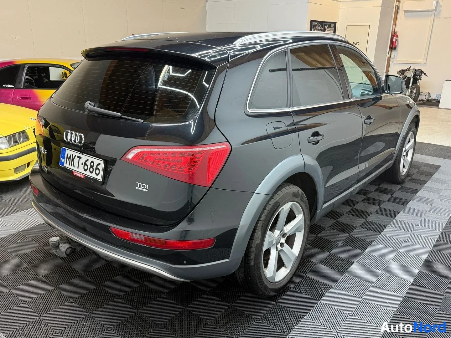 Takaviisto: Musta Audi Q5 takaa viistosti hallissa: takavalo, TDI-merkintä ja rekisterikilpi, pakokoukku asennettuna.