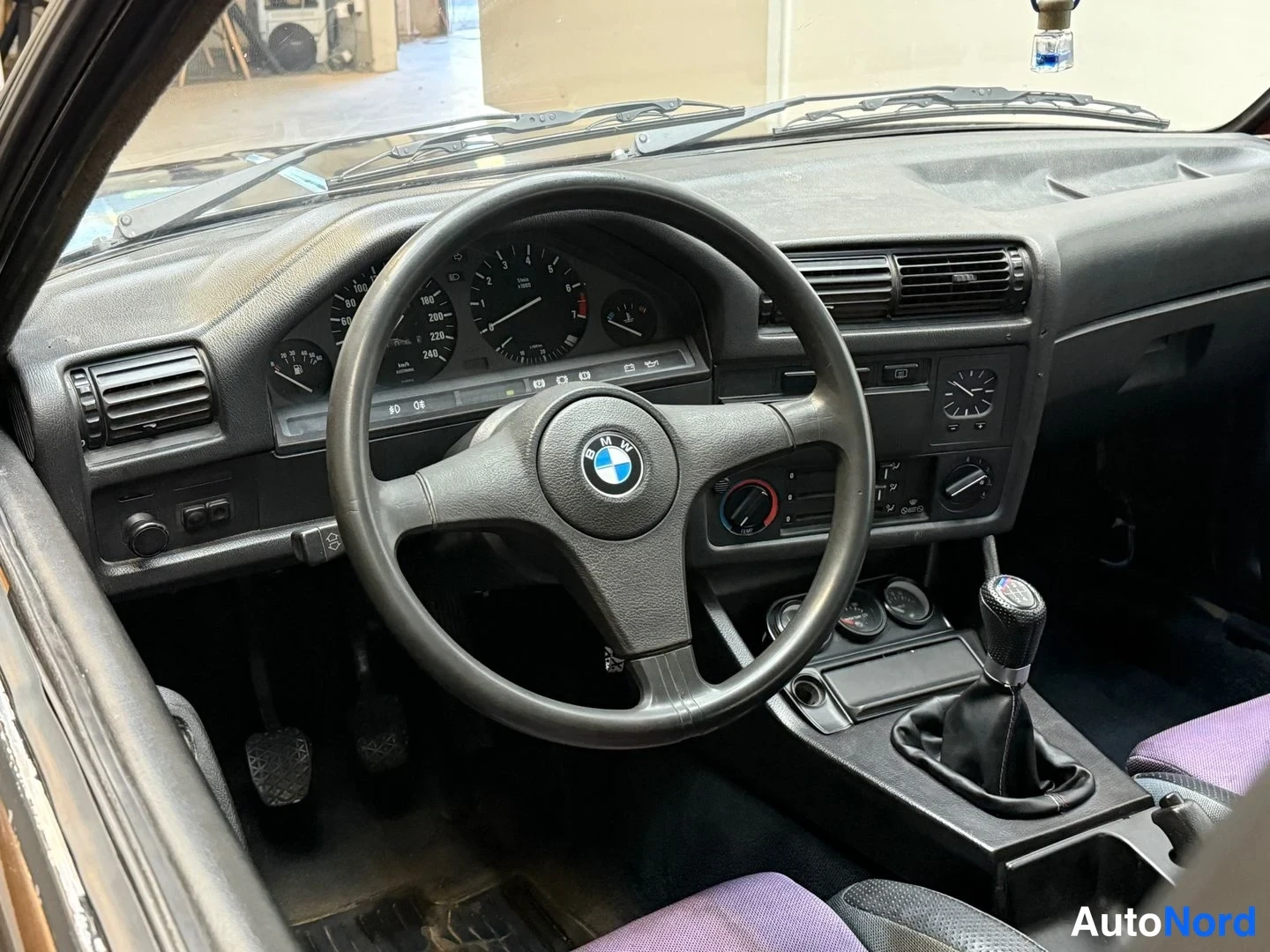 Sivulta: BMW:n ohjaamo: kolmipuolainen BMW-ohjauspyörä, analogiset mittarit, käsijarru ja manuaalivaihteen keilaus kuppipenkkiin.