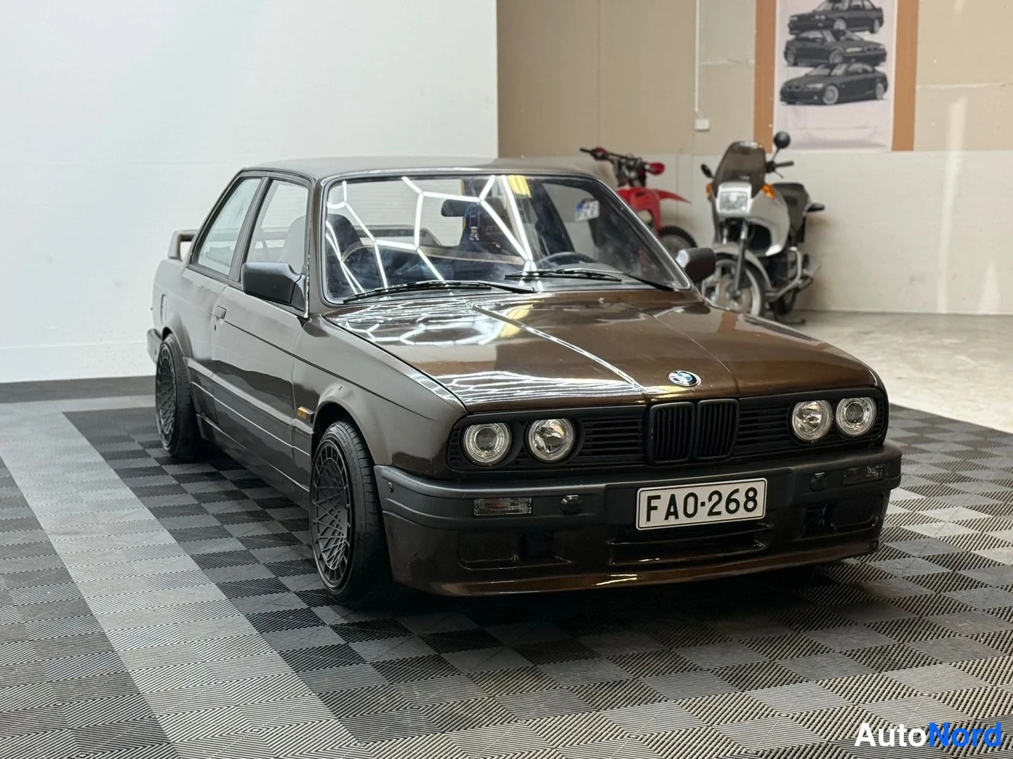 Etuviisto, nokka oikealle: Ruskea BMW E30 -sedan etukulmassa lasikorjaamossa; pyöreät etuvalot, musta etupuskuri ja rekisterikilpi FA0-268.