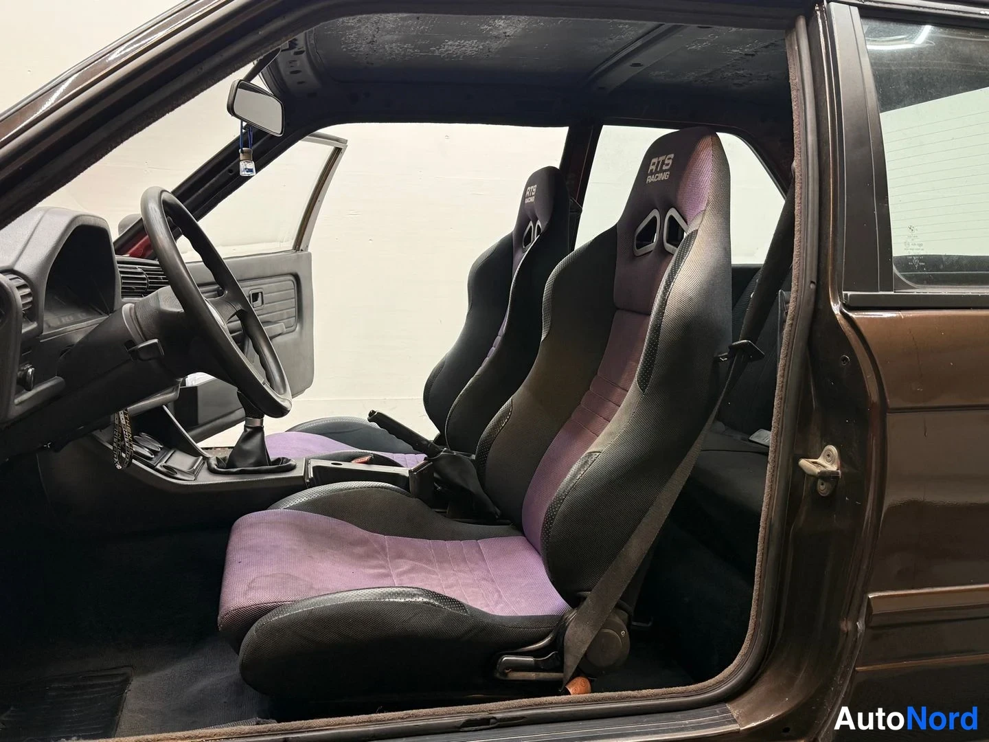 Edestä: Kaksi kilpailuistuinta (RTS Racing) musta-violetilla kankaalla, auto kuvattu avoimesta ovasta.