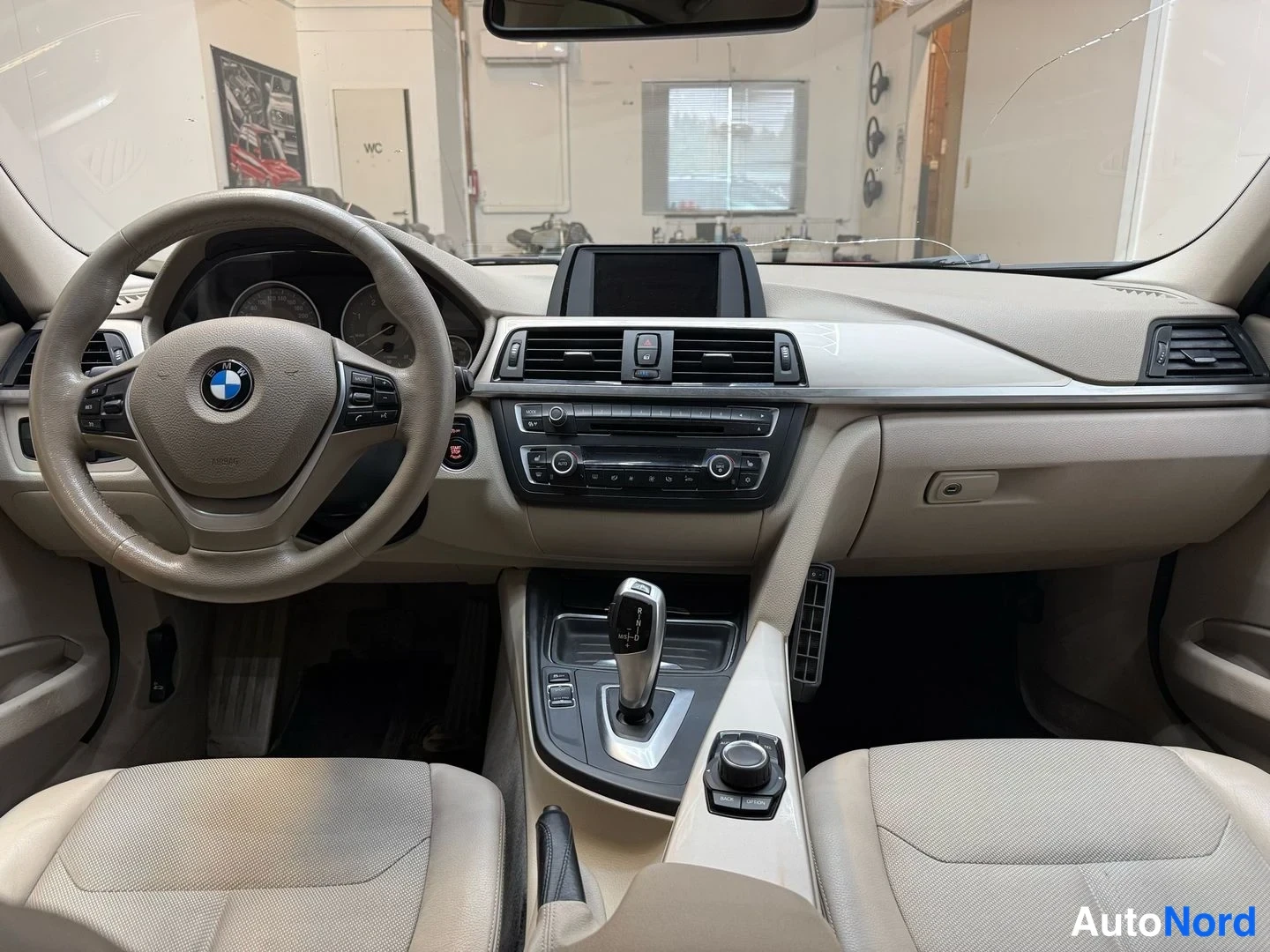Edestä: Auton sisätilat etupenkkien takaa kuvattuna: BMW-ohjauspyörä, hallintapaneeli, nesteytetyt istuimet ja automaattivaihteen valitsin.