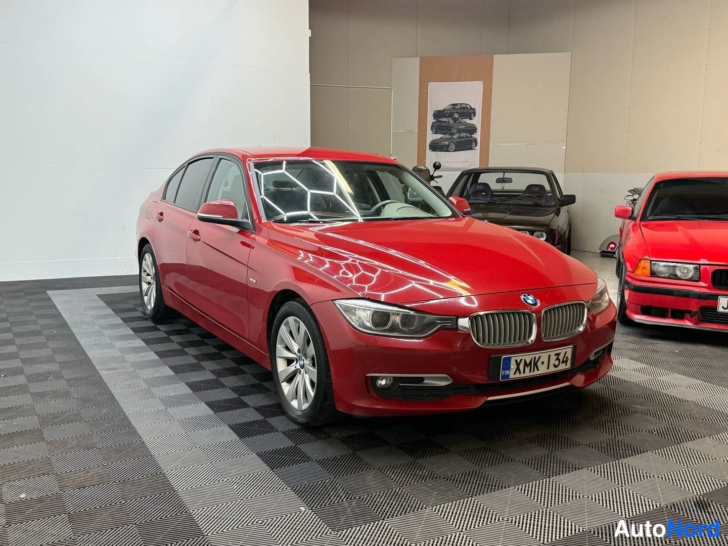 Etuviisto, nokka oikealle: Punainen BMW 3-sarjan sedan edestä oikealta kuvattuna autotallissa.