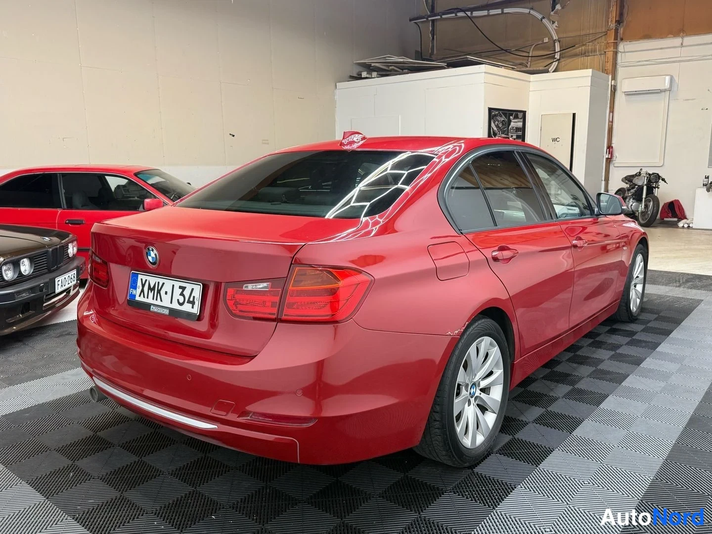 Takaviisto: Punaisen BMW-sedanin takakulmanurkku varastotilassa; takapaneeli, -rekisterikilpi ja oikea kylki näkyvät.