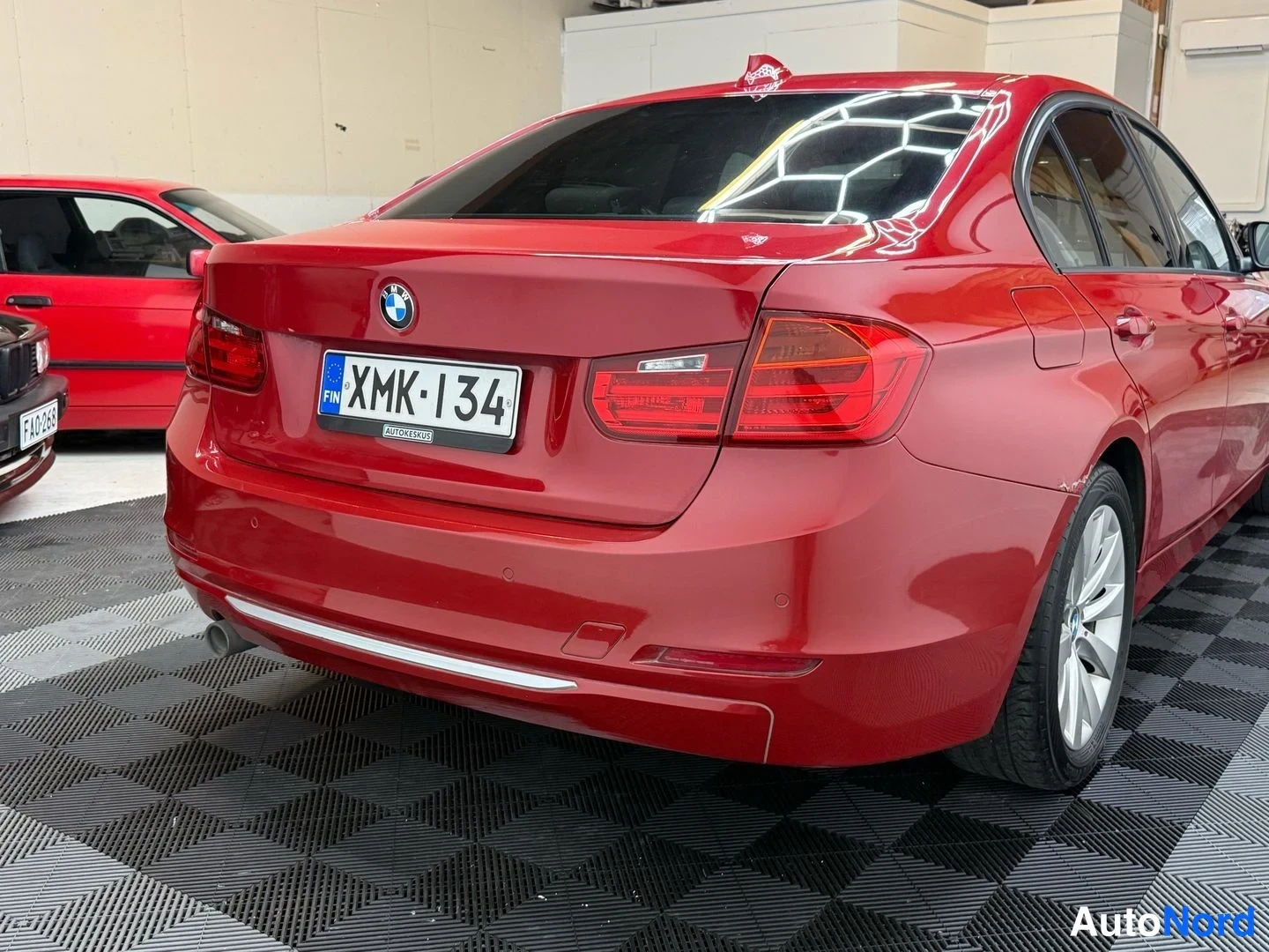 Takaa: Punaisen BMW-sedanin takaosa lähikuvassa; -rekisterikilpi, BMW-merkki ja takavalot näkyvät.