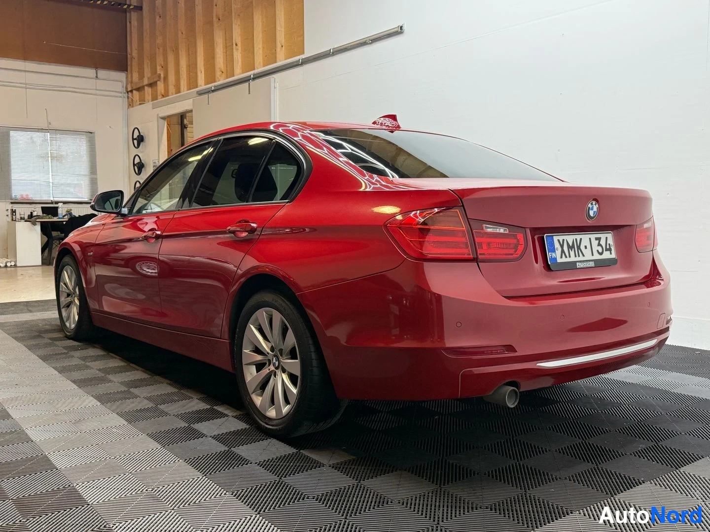 Takaviisto: Punaisen BMW-sedanin takakulmanurkku sisätilassa; takapaneeli, -rekisterikilpi ja vasen kylki näkyvät.