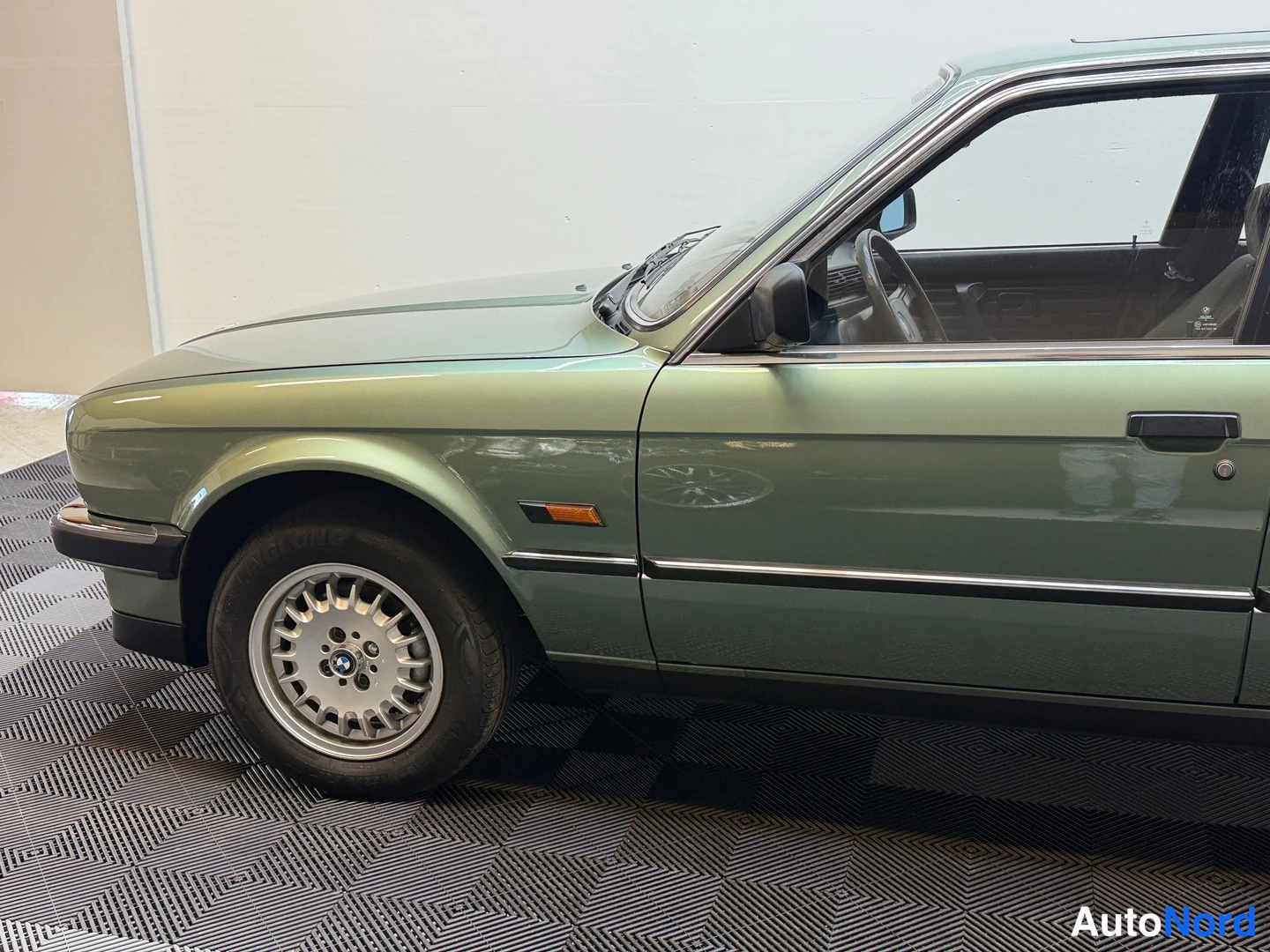 Etuviisto, nokka vasemmalle: BMW 324d etukulmasta vasemmalle, vihreä koripaneeli, etupyörä ja BBS-tyylinen vannekese näkyvät sisätiloissa.