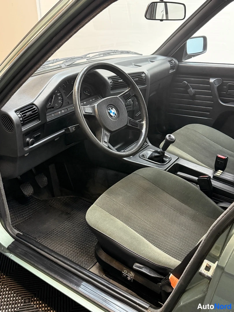 Muu: Auton sisätilat ohjaamosta: BMW-ohjauspyörä, analogiset mittarit, manuaalivaihteen keppi ja vihreät kankaanistuimet.