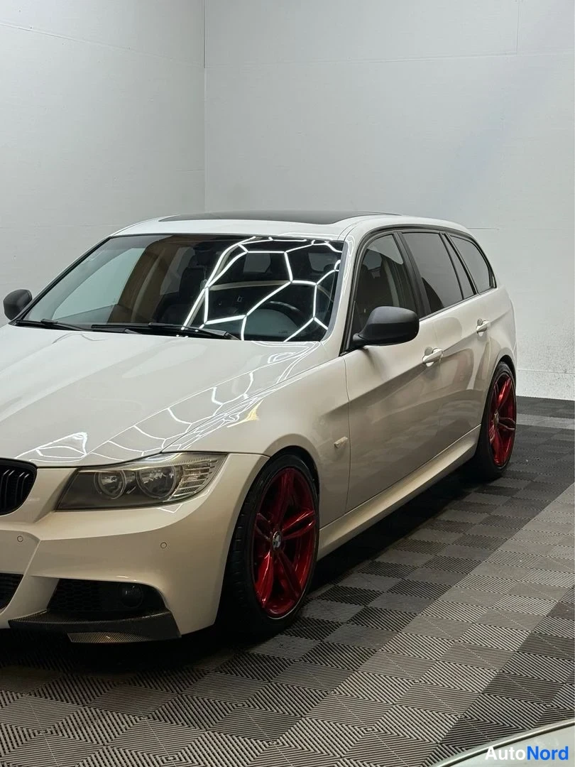 Etuviisto, nokka vasemmalle: Valkoinen BMW-farmari etukolmasosa vasemmalla, punaiset vanteet, sisätiloissa.