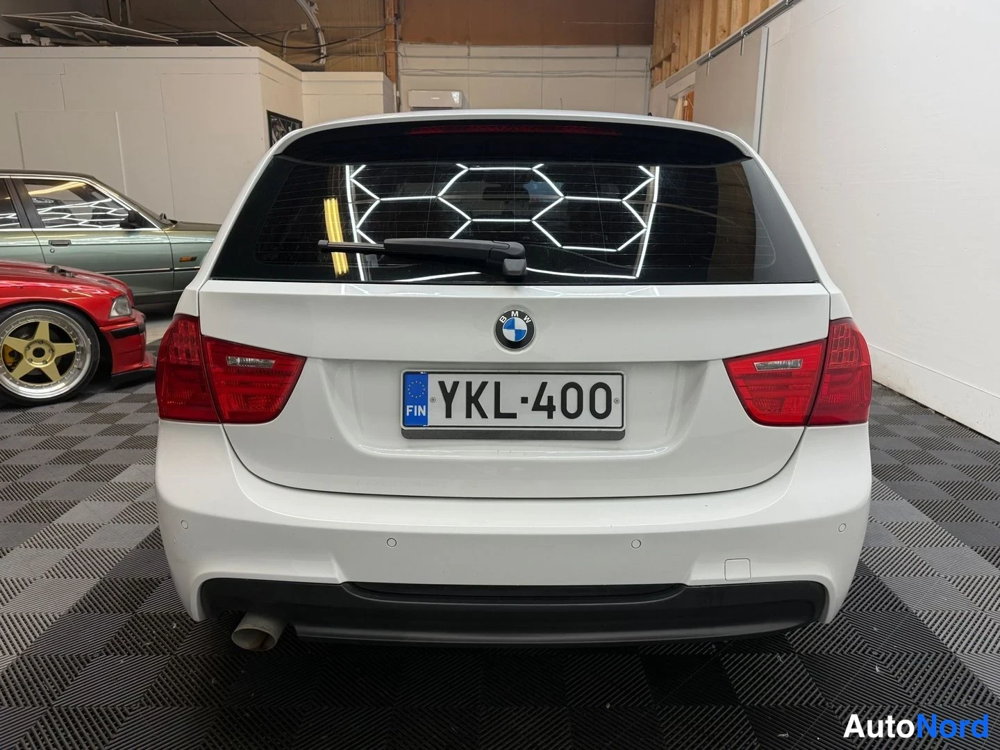 Takaa: Valkoinen BMW-farmariauto suoraan takaa kuvattuna, rekisteritunnus, punaiset takavalot, takatölkki ja difuuseri.