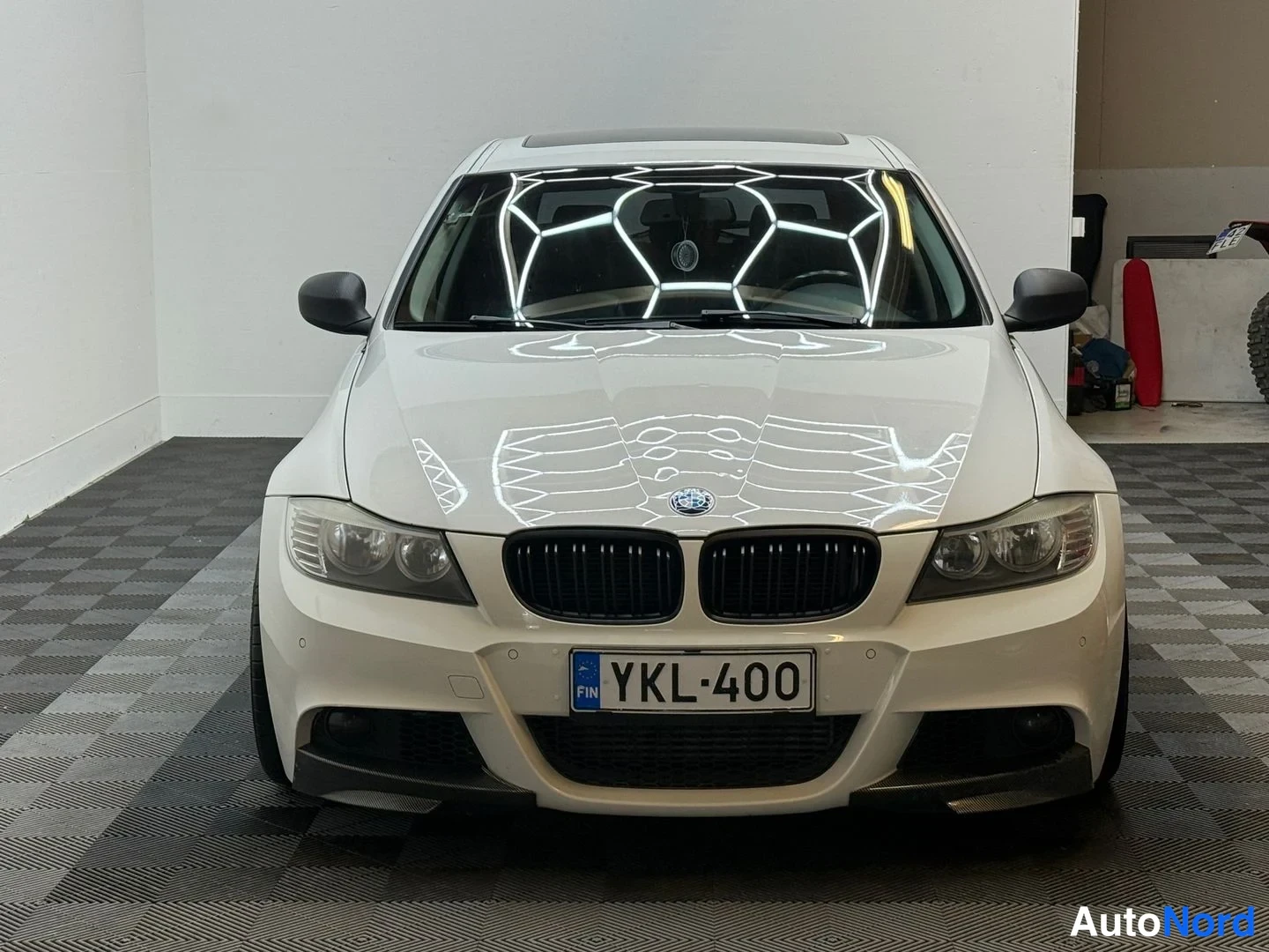 Edestä: Valkoinen BMW suoraan edestä, musta etugrilli, -rekisterikilpi ja lasikatto näkyvissä sisätiloissa.