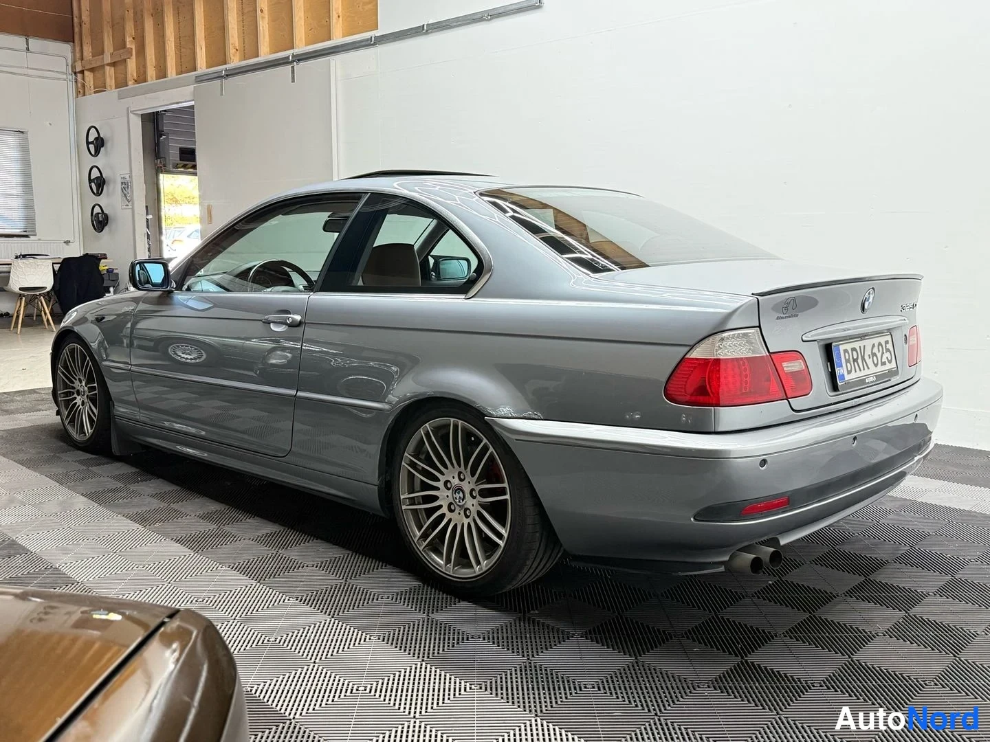 Takaviisto: Hopeanharmaa BMW-coupé takalusta ja vasemmasta sivusta kuvattuna, rekisterikilpi, beigen sisäistit hieman näkyvissä.