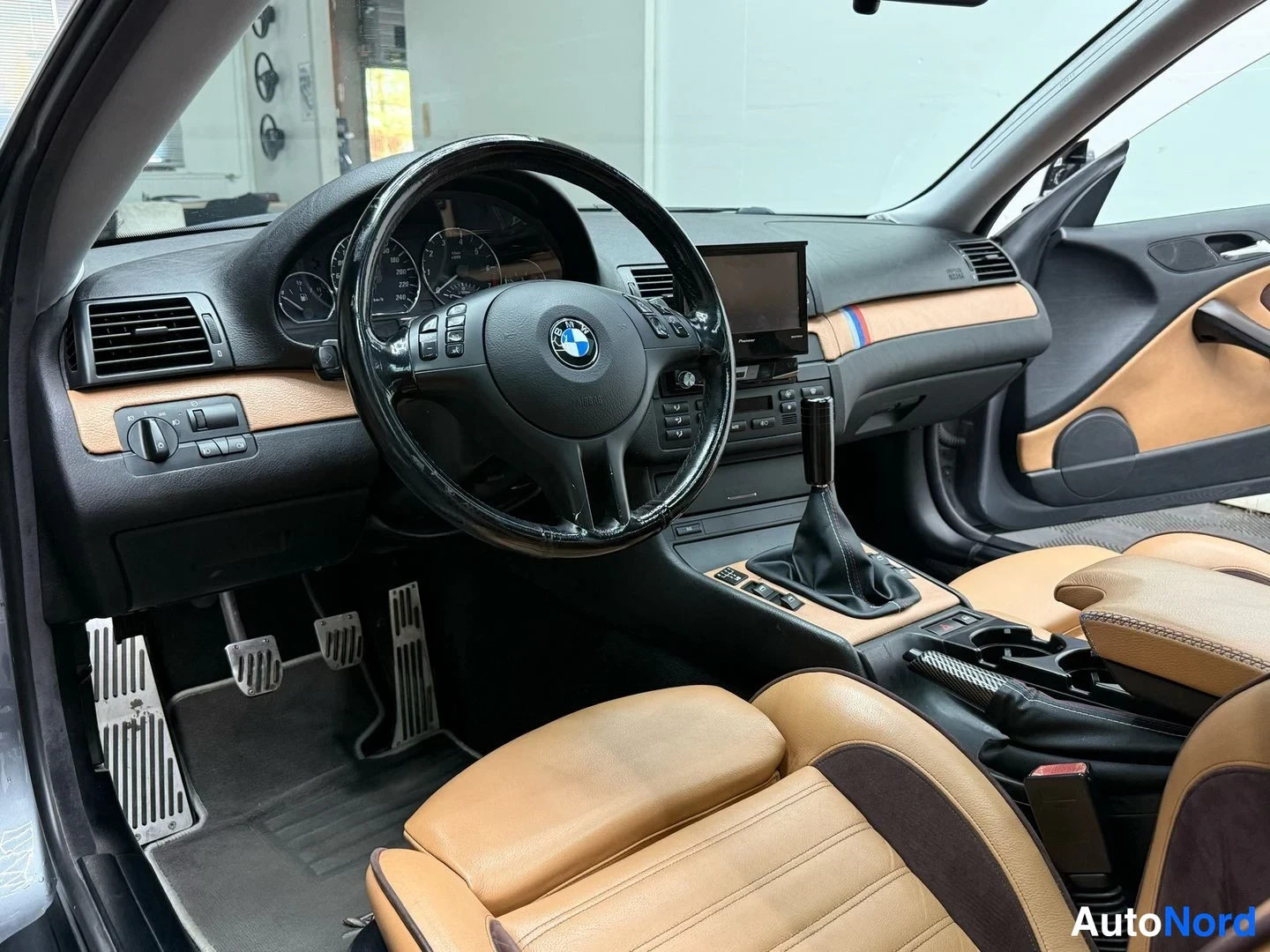 Sivulta: Auton sisätilasta kohti ohjauspöytää ja kojetaulua, BMW-ohjauspyörä, tan-nahkaiset penkit, manuaalivaihtoheinä ja alumiiniset polkimet.