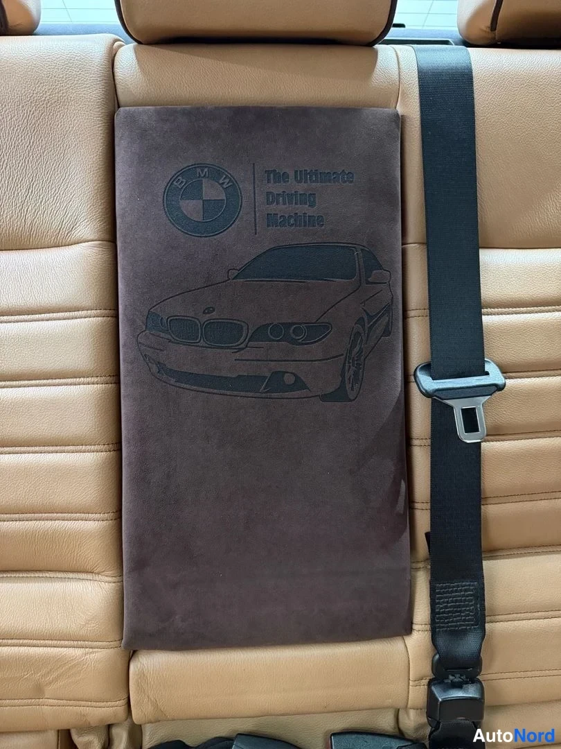 Muu: Tummanruskea suojakansin peitetty BMW-ohjekirja takaistuimen keskellä; kansessa BMW-logo, auton kuva ja teksti 'The Ultimate Driving Machine'.