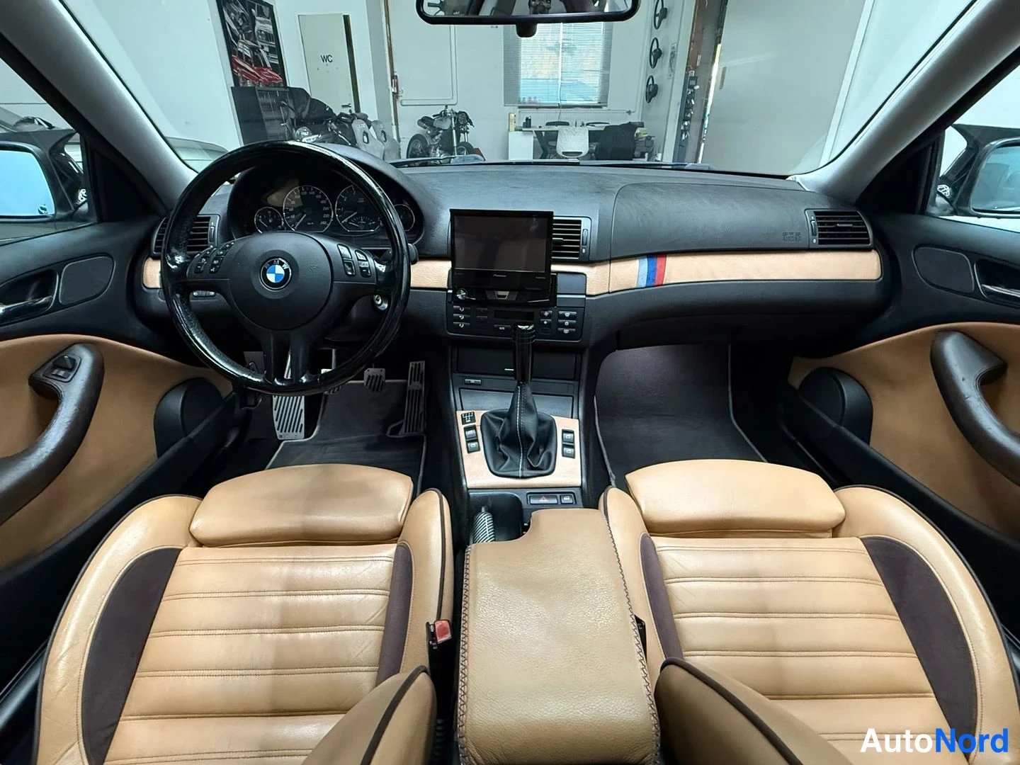 Takaa: Auton sisätilat etupenkeiltä kuvattuna: beige-nahkaiset urheiluistuimet, BMW-ohjauspyörä, mitat, vaihtokeppi ja dashboardiin asennettu Pioneer-näyttö.