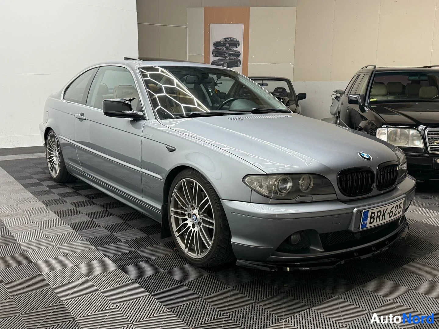 Etuviisto, nokka oikealle: Hopeanharmaa BMW-coupé etukulmasta sisätiloissa, rekisterikilpi.