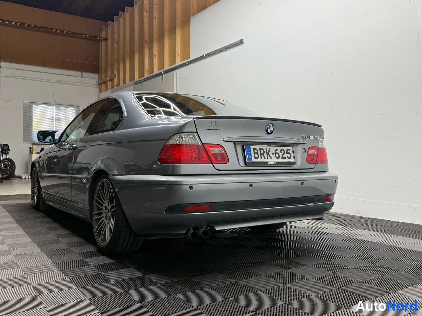 Takaviisto: Hopeanharmaan BMW-coupén takaosa suoraan takaa kuvattuna, rekisterikilpi, kaksiosainen pakoputki ja tasaantumispaneelit näkyvät.