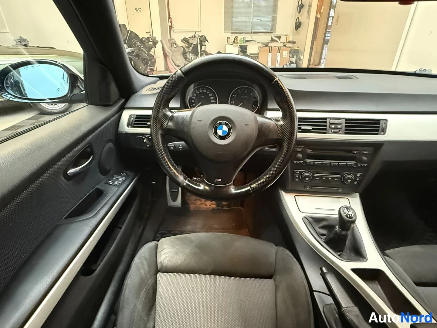 Yksityiskohta: Kuljettajan puolen näkymä: BMW-M-ohjauspyörä, analogiset mittarit, manuaalivaihtokeppi ja keskihallinnon säätimet.