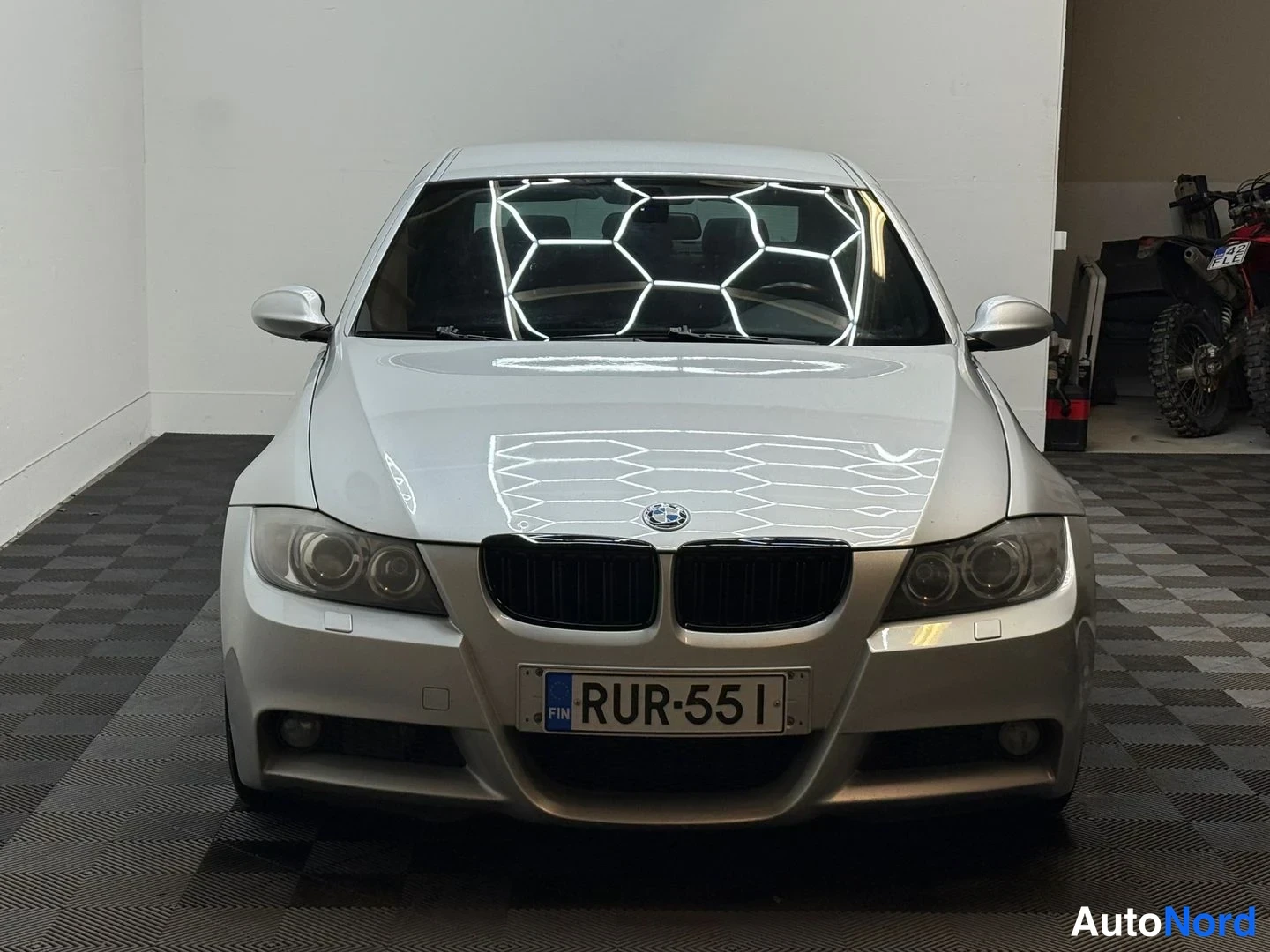 Edestä: Hopea BMW-sedan suora edessäpäin kuvattuna sisätiloissa.