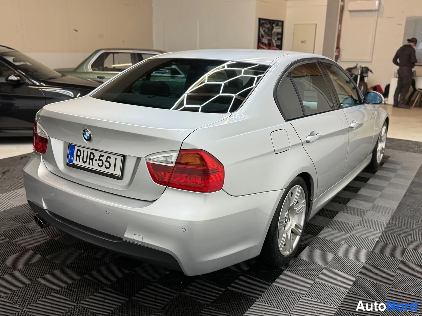 Takaviisto: Hopea BMW-sedan takaa sivusuunnassa: takavalot, pohja ja D-vaihteen puoleinen kylki; rekisteritunnus.