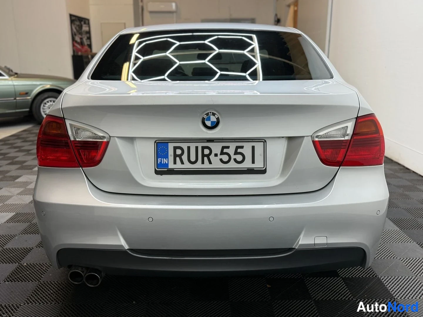 Takaa: Auton takaosa suoraan takaa: BMW-merkki, eurooppalainen rekisterikilpi ja punaiset takavalot hopeanvärisessä korissa.