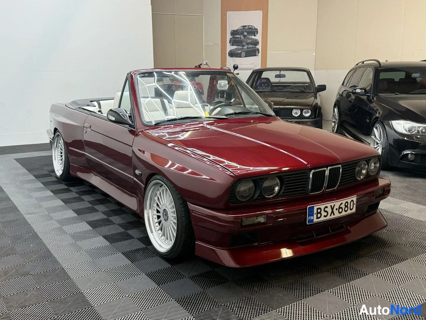 Etuviisto, nokka oikealle: Punametallin värinen BMW 325i Cabriolet -avolava etuviistossa oikealle, rekisteritunnus, katto auki, hopeat renkaiden vanteet.