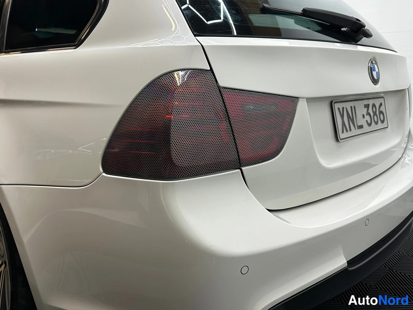 Takaviisto: Valkoisen auton takasivu ja takaluukku: tummat takavalot, BMW-tunnus ja rekisterikilpi.