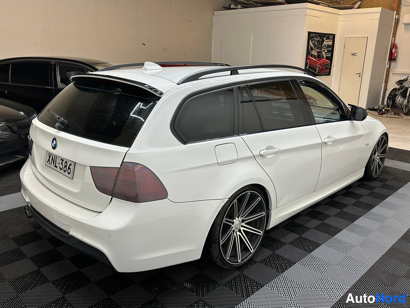 Takaviisto: Takakulmanäkymä valkoisesta BMW-farmarista, takavalo tummennettu, rekisterikilpi.