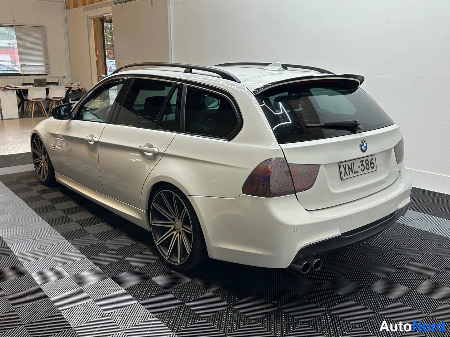 Takaviisto: Takakulmanäkymä valkoisesta BMW-farmarista sisätilassa, rekisterikilpi ja kattokaiteet.
