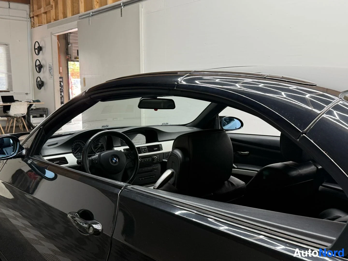 Muu: Mustan avoauton kuljettajan puolen näkymä sisätiloihin, BMW-ohjauspyörä, mittaristo ja mustat istuimet näkyvät.
