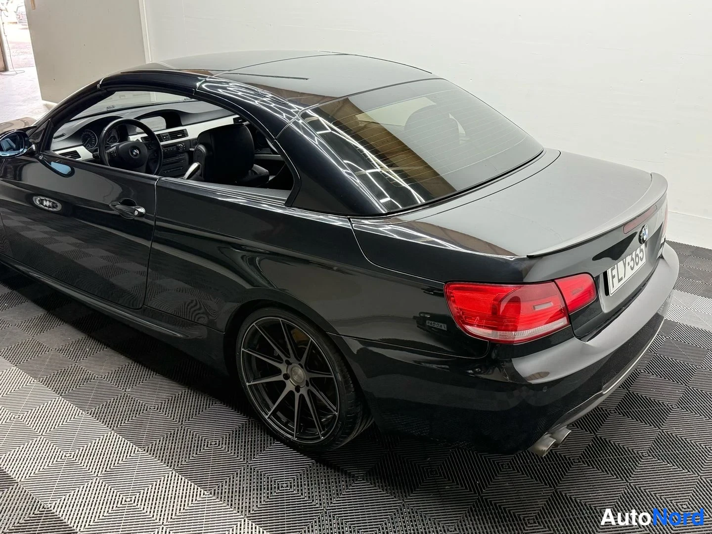 Takaviisto: Mustan avomallin BMW:n takakulman näkyvä sivutakaview: valmistettu takavalot, musta kori ja rekisterikilpi kuvattu sisätilassa.