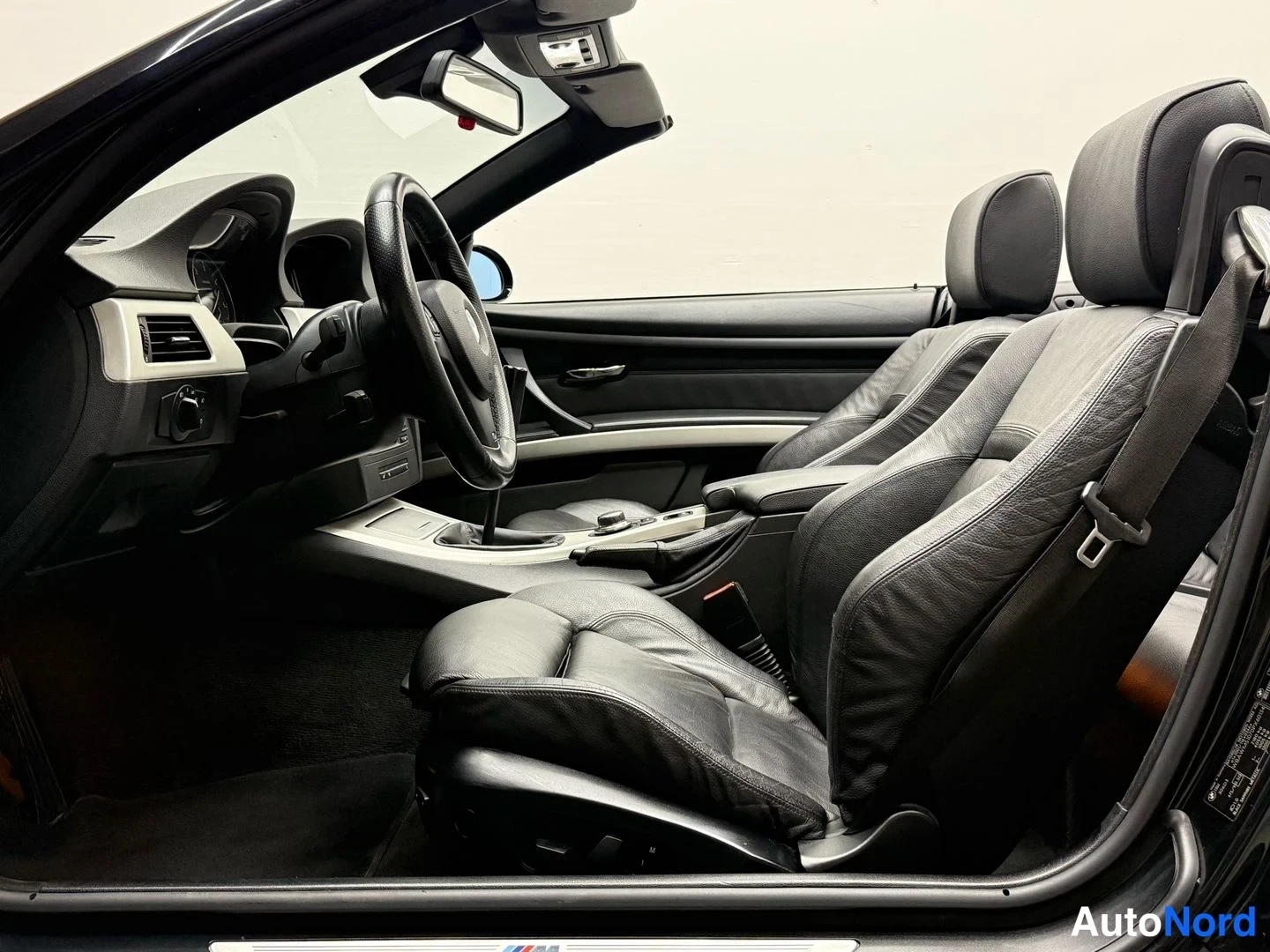 Sivulta: Sisäkuva mustan BMW:n etupenkistä, ohjauspyörä ja kojelauta näkyvät.