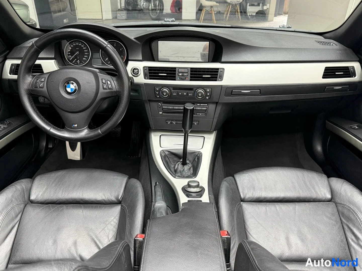 Sivulta: Sisätilakuva ohjaamosta: BMW-ohjauspyörä, analogiset mittarit, manuaalivaihtajan mukaan lukien keskikäyttöpöydän näyttö, mustat nahkaistuimet ja hopeanväriset k