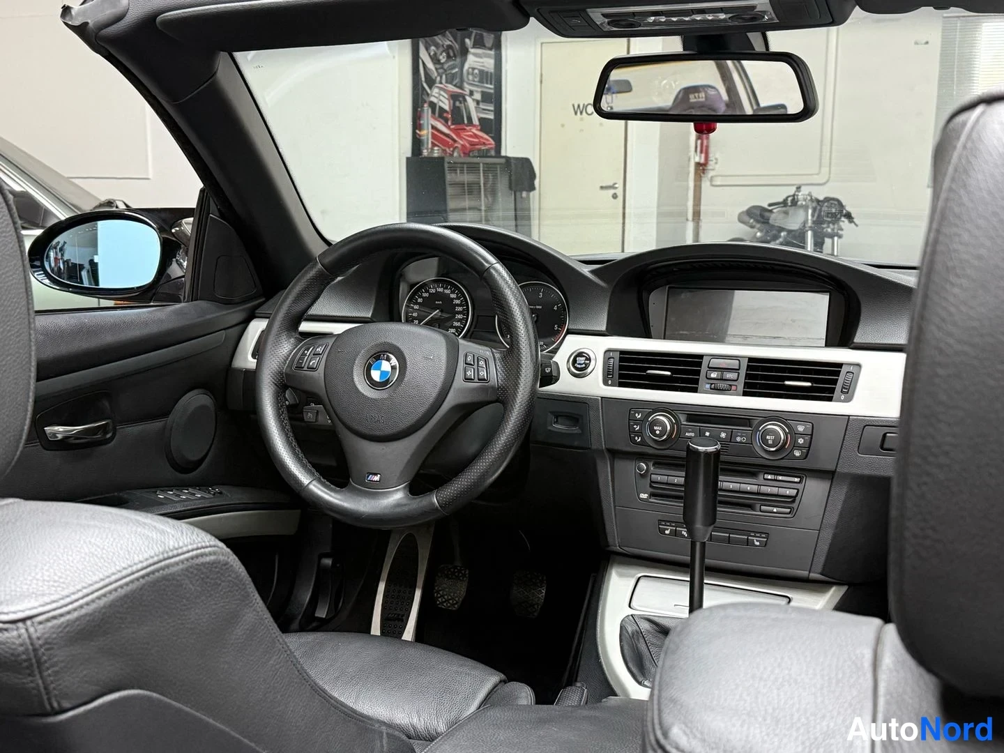 Sivulta: Ohjaamo avoautona pehmikatto auki: BMW-M-ohjauspyörä, mittarit, keskikäyttöpöydän näyttö ja säätimet, mustat nahkaistuimet, takaa istuinosat osin kuvassa.