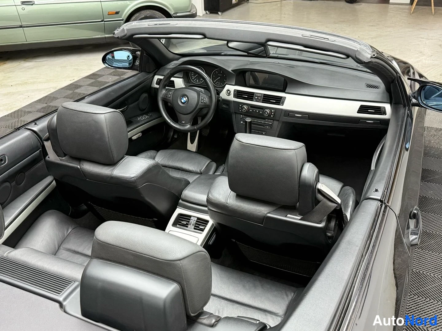 Sivulta: Mustan avoauton sisätilat peilitetty: ratissa BMW-merkki, mustat nahkaistuimet, kojetaulu ja keskikonsoli näkyvät.