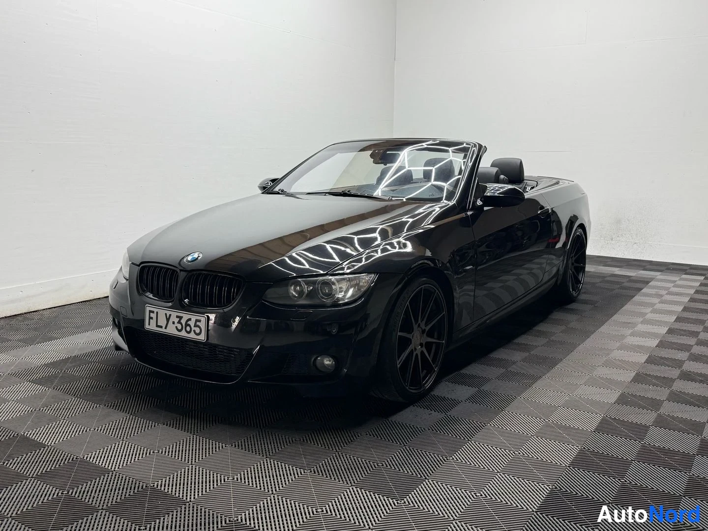 Etuviisto, nokka vasemmalle: Musta avokattoinen BMW-urheiluauto etukulmasta vasemmalta, rekisteritunnus, mustat vanteet, koroton katto.