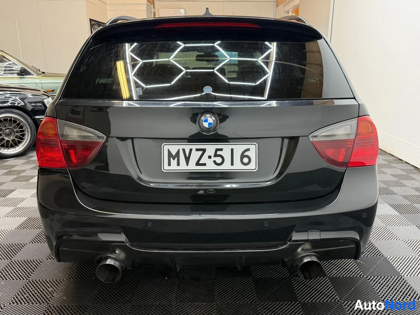 Takaa: Mustan farmariauto suora takaa, rekisteritunnus, punaiset takavalot ja kaksoispakoputket.
