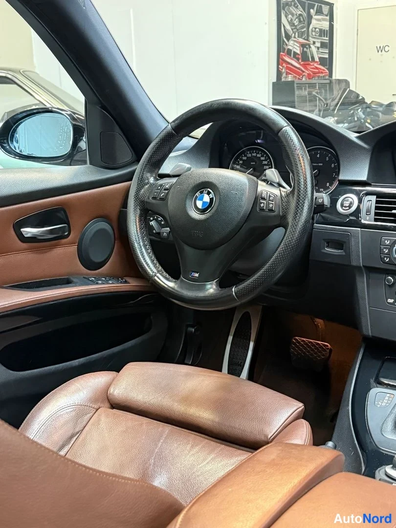 Muu: Lähikuva ohjauspyörästä ja kojelaudasta, BMW-logo ohjauspyörässä, ruskea nahkaistuin etualalla.