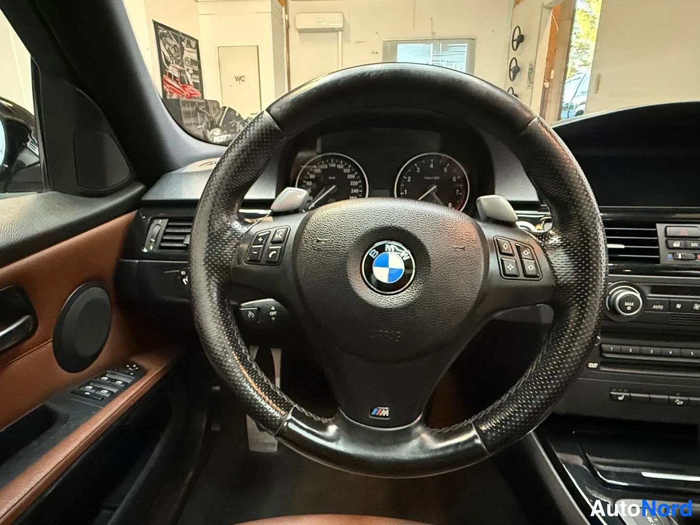 Etuviisto, nokka oikealle: Ohjauspyörä ja mittaristö sisältä; BMW-merkki ja M-logo ohjauspyörässä, vaihdinpypylät ja kojelaudan painikkeet näkyvissä.