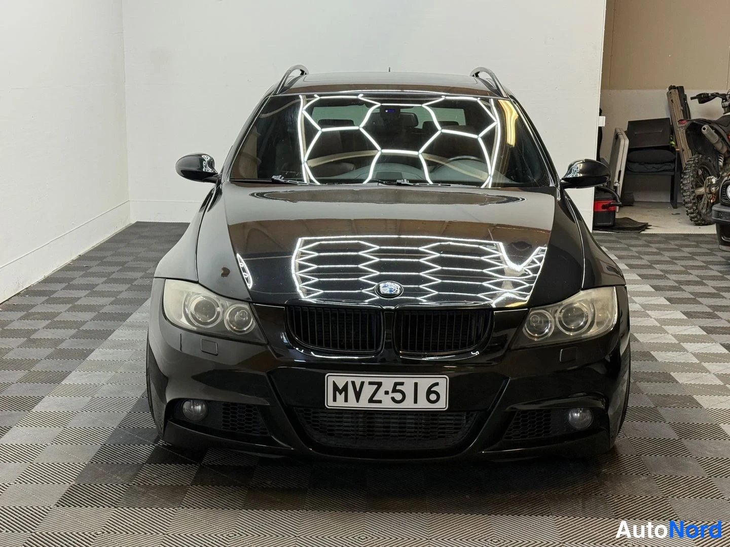 Edestä: Mustan BMW-farmariauton suora etunäkymä, rekisteritunnus, kattokaiteet näkyvissä.
