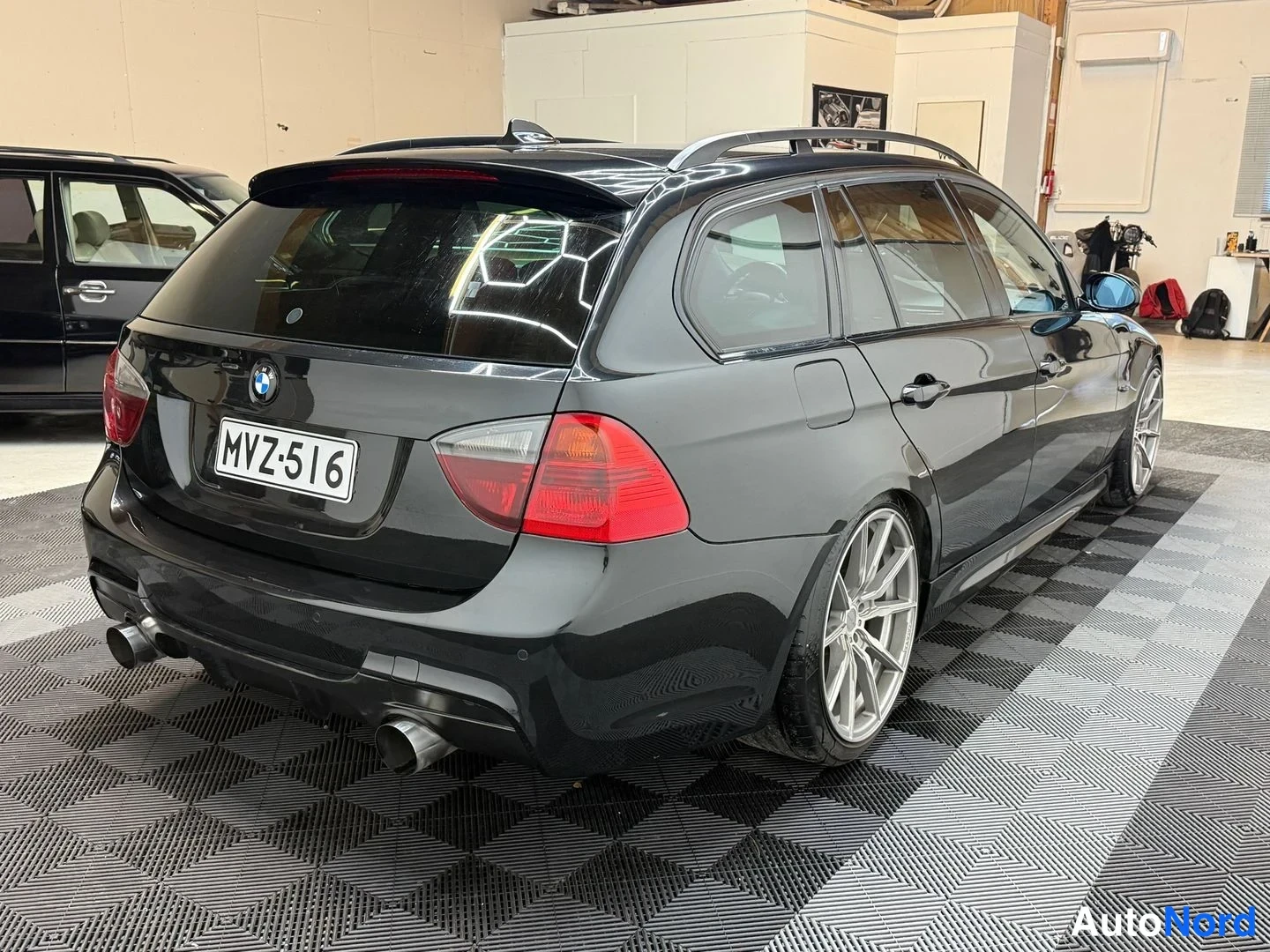 Takaviisto: Mustan farmariauto takakulma takaa-oikealta, rekisteritunnus, hopeat monivaraminnit ja kaksoispakoputki.