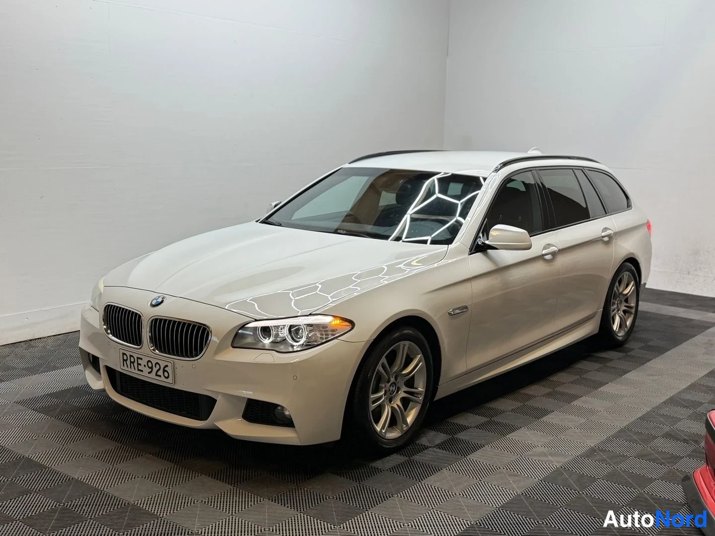 Etuviisto, nokka vasemmalle: BMW 525d -farmariauto etuosa ja vasen sivu näkyvät kuvakulmasta, valkoinen korimaali, rekisterikilpi, studiohuoneessa.