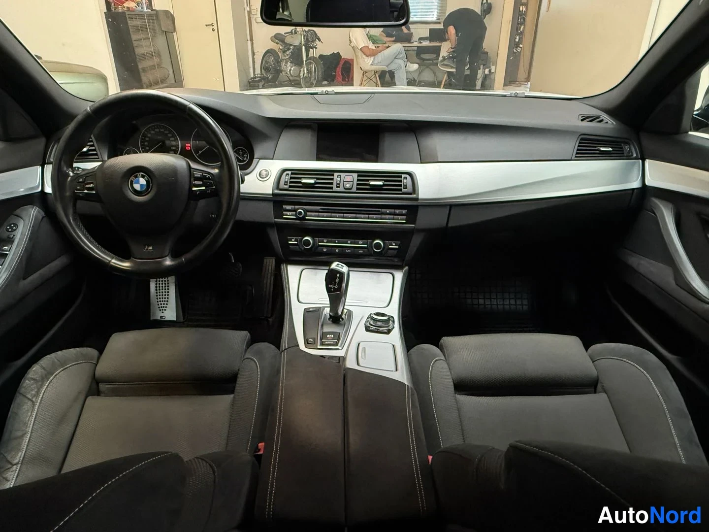 Edestä: Sisätilat eteenpäin: BMW-ohjauspyörä, musta kojelauta ja vaihtoautomaatin valitsin.