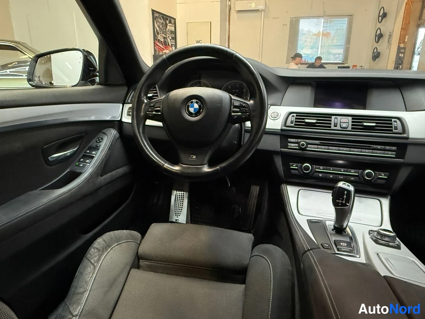 Muu: Auton sisätilat: BMW-ohjauspyörä, automaattivaihdevalitsin, kojelaudan näyttö ja tummat istuimet.