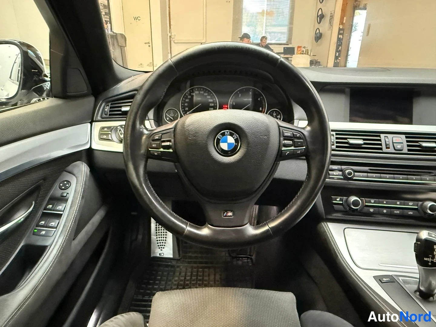 Edestä: Ohjaamo näyttää kojelaudan, BMW-ohjauspyörän ja mittaristön.