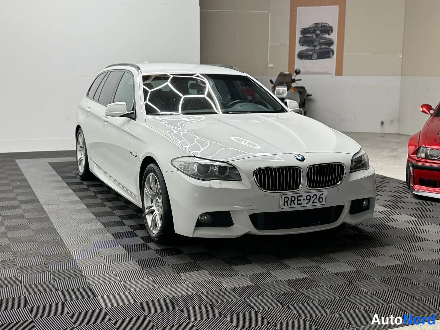 Etuviisto, nokka oikealle: Etukolmanneltakulma valkoisesta BMW-farmariautosta, keulakoriste ja -rekisterikilpi näkyvissä.