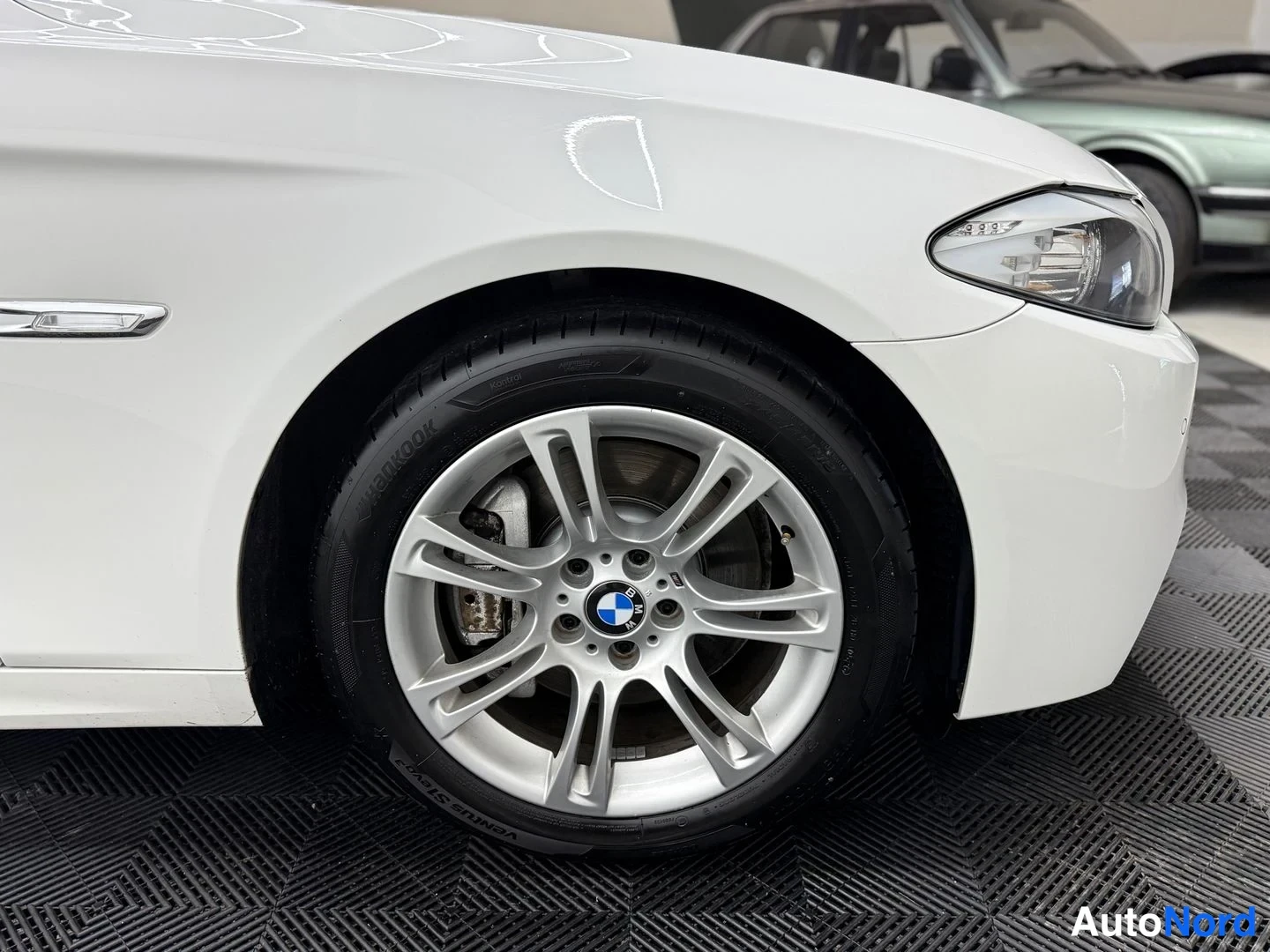 Etuviisto, nokka oikealle: BMW 5 Touring -Auton etuosan kolmeneljänneskuva oikealta; hopeavanne ja etusumuvalo näkyvät