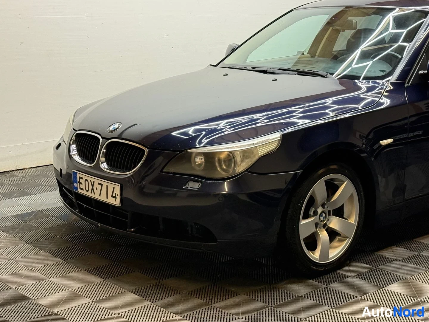Etuviisto, nokka vasemmalle: Lähikuva sinisen BMW-sedanin keulasta ja etupyörästä vasemmalta, rekisterikilpi ja keulakoristeena BMW-merkki.